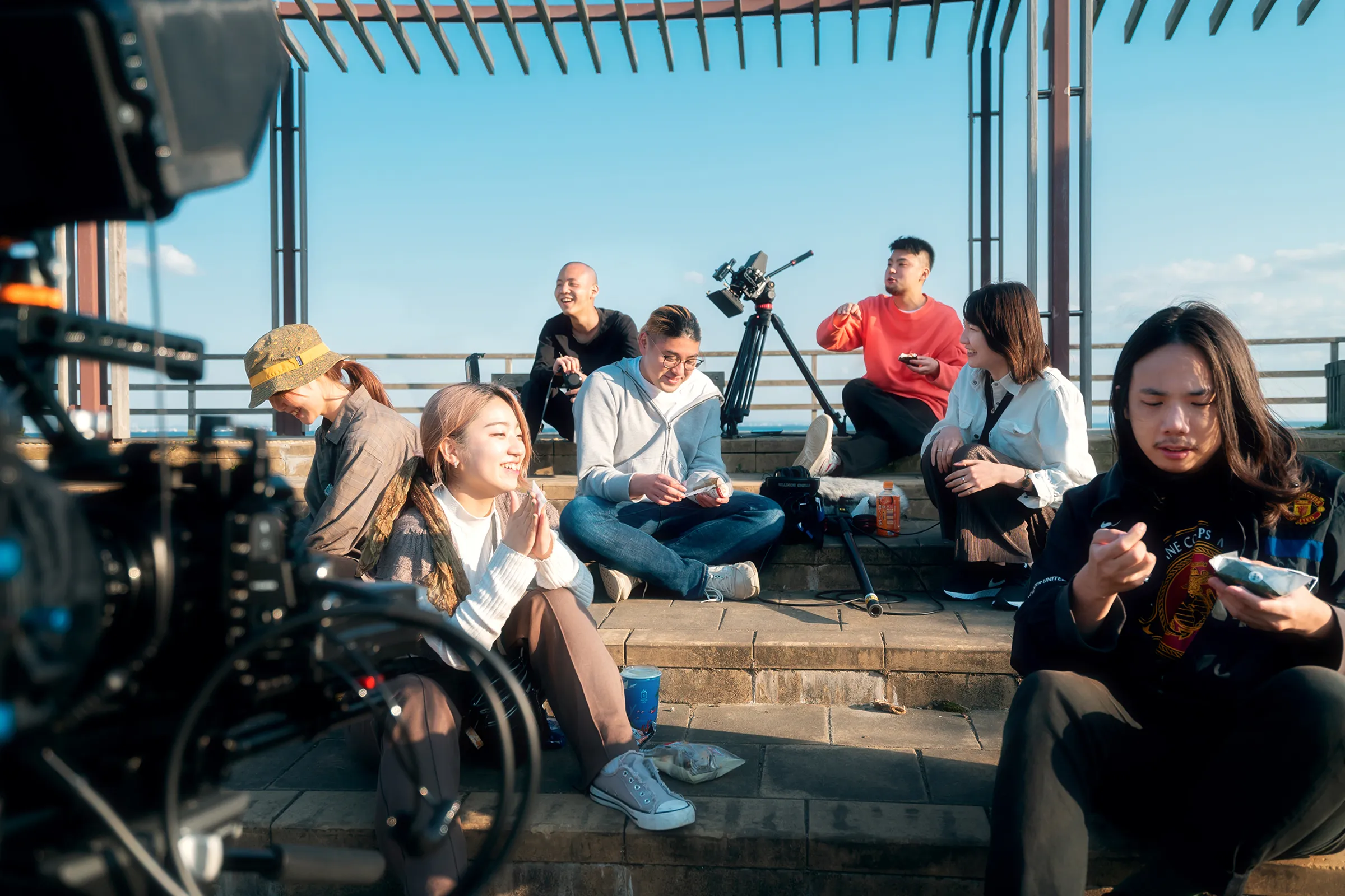 FIXVILLE crew taking a break on outdoor stone steps during a film shoot, with cinema cameras and a boom microphone nearby.
